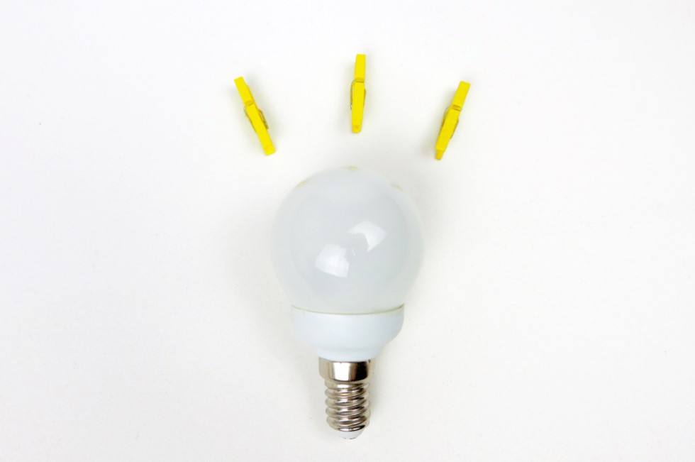 Lightbulb on white background surrounded by three yellow clothes pegs