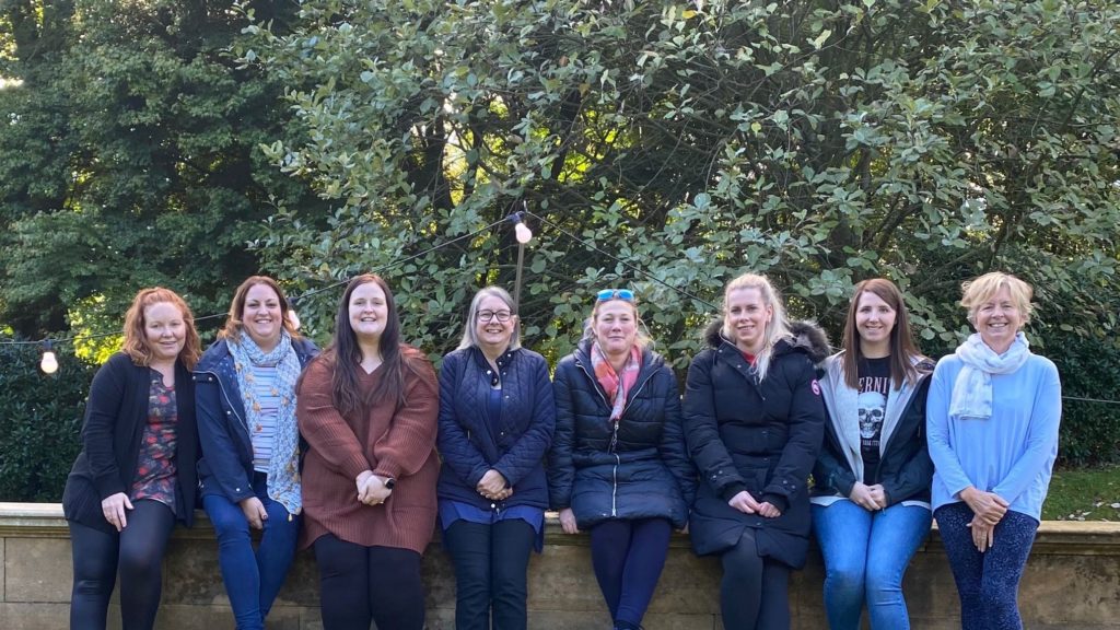 Eight people sitting on a ledge in front of trees